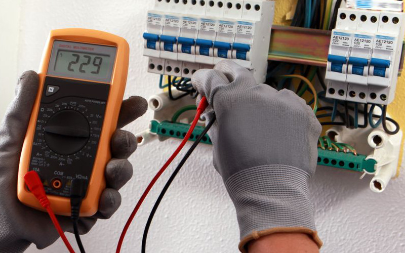 Elektriker misst mit einem Multimeter die Spannung in einem Sicherungskasten für Elektroinstallation.